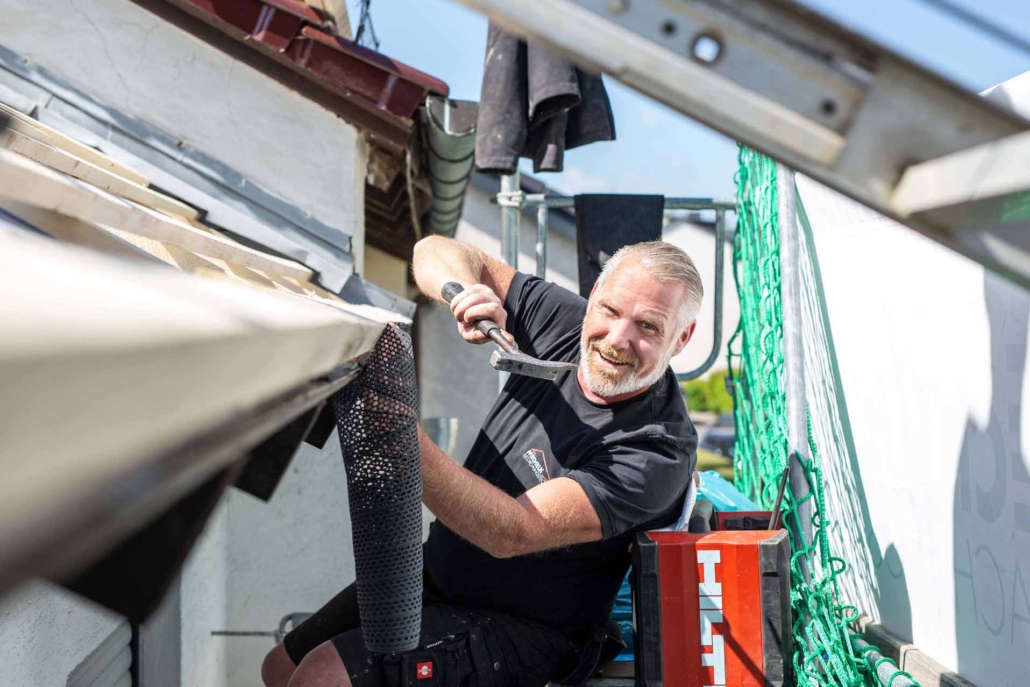 Lachender Dachdecker befestigt Gitter an Dachrinne