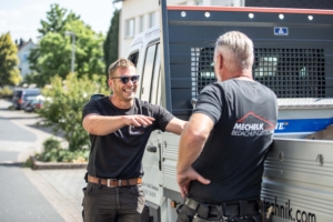 Zwei Dachdecker unterhalten sich lachend am Firmenfahrzeug