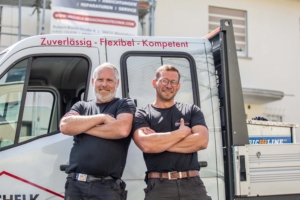 Zwei Dachdecker stehen mit verschränkten Armen vor Transporter