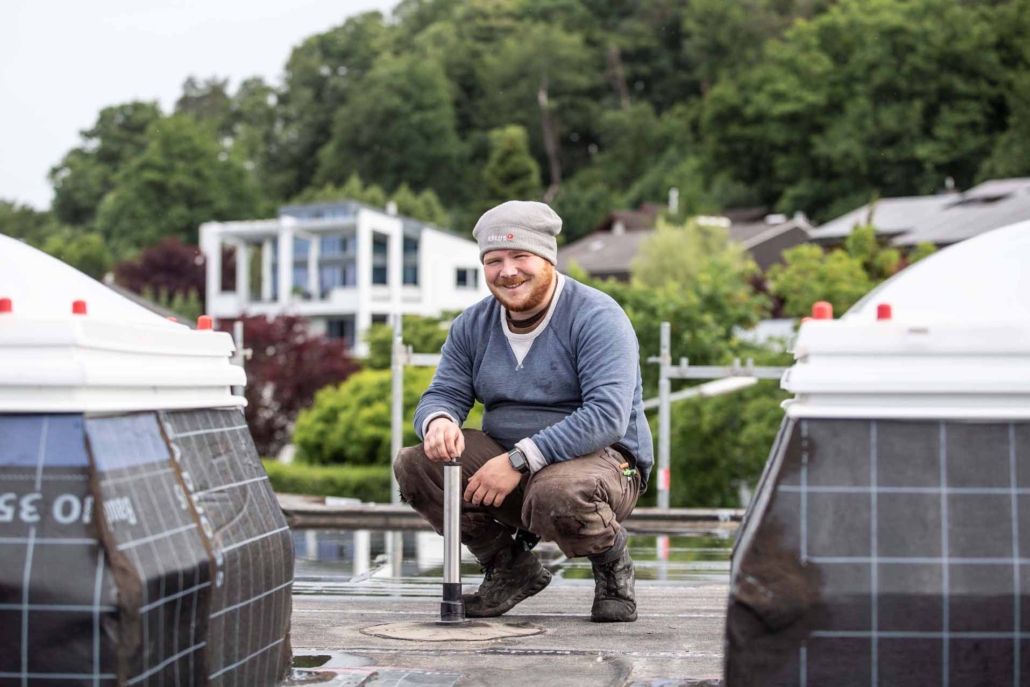 Gute Laune auf dem Dach Dachdecker mit Mütze kniet lachend auf Flachdach