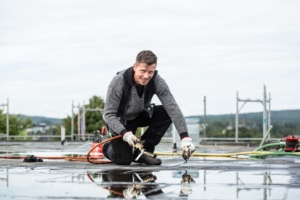 Dachdecker arbeitet lachend mit Brenner auf nasser Dachfläche