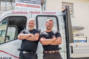 Zwei Dachdecker stehen mit verschränkten Armen vor Transporter